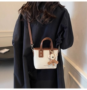 Detail einer beige-braunen Eimertasche mit Affenanhänger, getragen von einem Model