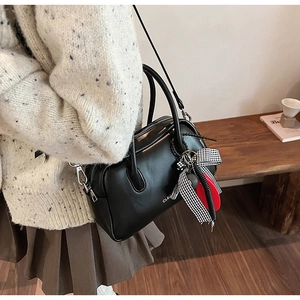 Detalle de un bolso Boston vintage de cuero negro con cinta de cuadros y colgante rojo