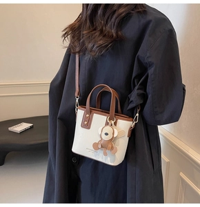 Detail der cremefarbenen PU-Mini-Tasche mit braunen Kontrastriemen und Affen-Anhänger