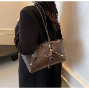 Detail of a dark brown leather tote bag with knotted cords and slim gold hardware