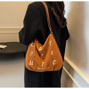 Close-up of orange-brown corduroy tote bag featuring white embroidered letters and fine strap