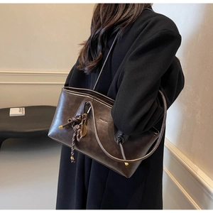 Detail of dark brown faux leather tote with drawstring design and gold tennis racket charm