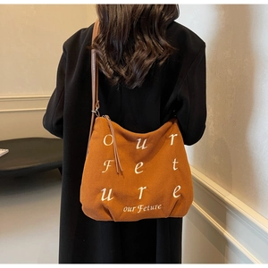 Detail of caramel corduroy tote bag featuring white embroidered letters and slim leather straps