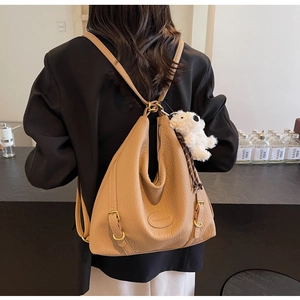 Khaki pebbled leather convertible backpack with gold rings and plush charm on a model