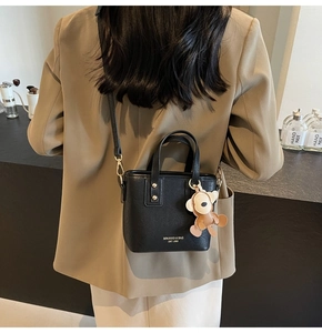 Detail einer schwarzen Mini-Handtasche mit goldener Hardware und süßem Bärenanhänger