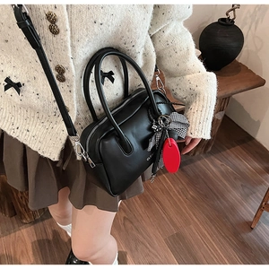 Detalle de bolso Boston de cuero negro con lazo y correa ajustable llevado por una modelo