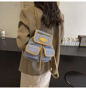 Détail du sac à dos en jean avec logo doré, bordure en cuir et bretelles en chaîne