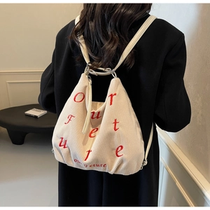 Detail of beige corduroy backpack featuring red embroidered text and white shoulder straps