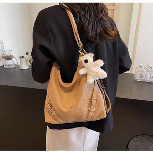 Close-up of khaki pebbled leather shoulder bag with gold buckles and plush bear charm