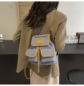 Détail d'un sac à dos en denim bleu avec bordures en cuir brun et bretelles en chaîne
