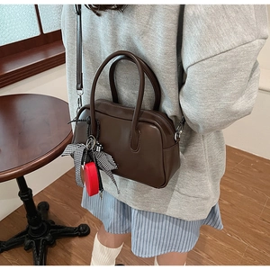Detalle de bolso Boston de cuero marrón oscuro con cinta decorativa y hebilla metálica