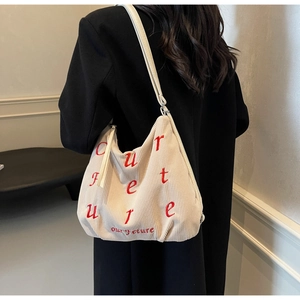 Macro detail of creamy corduroy tote bag with red embroidered letters and zipper closure