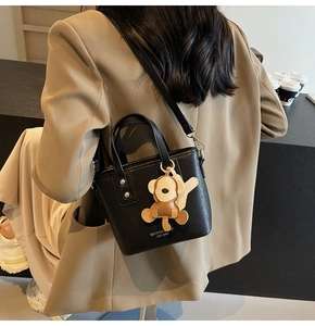 Detail einer schwarzen Leder-Beuteltasche mit Affenanhänger und weißem Markenlogo am Model