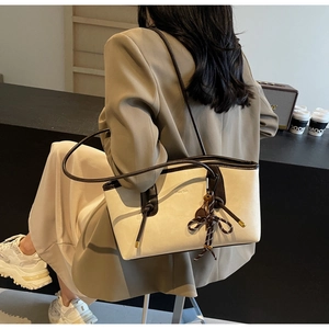 Detail of a cream faux leather tote bag with brown straps and woven tassel pendant