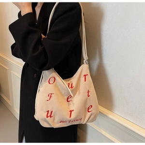 Close-up of beige corduroy tote bag with red embroidery and leather straps detail