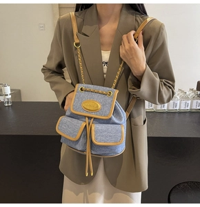 Détail du sac à dos en denim bleu clair avec garniture en cuir brun et détails dorés