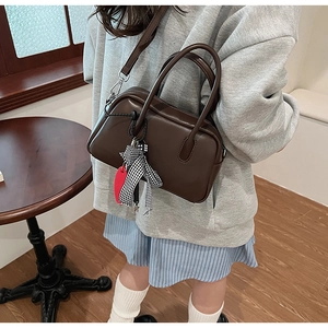 Detalle de bolso bandolera marrón oscuro con lazo de cuadros y colgante de corazón