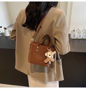 Braune Leder-Eimertasche mit verstellbarem Gurt und Affen-Anhänger am Modell gezeigt