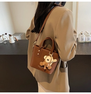Detailansicht einer braunen Eimertasche aus Leder mit Bärenanhänger und Logodruck