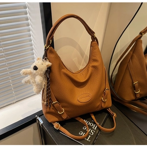 Close-up of brown pebbled faux leather bag with adjustable straps and plush bear charm
