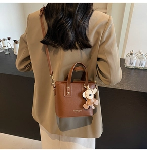 Detail einer braunen Ledertasche mit Plüschbären-Anhänger und Umhängeriemen