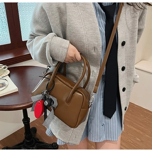 Primer plano de bolso Boston en cuero marrón con elegante lazo y colgante de esfera