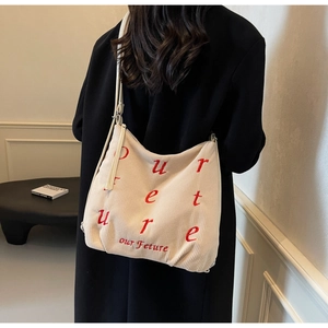 Detailed view of beige corduroy tote bag with red letter embroidery and slim shoulder strap