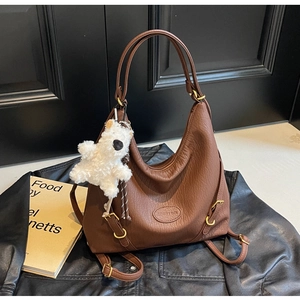 Detail of a brown leather hobo bag with a plush bear charm on a black leather jacket