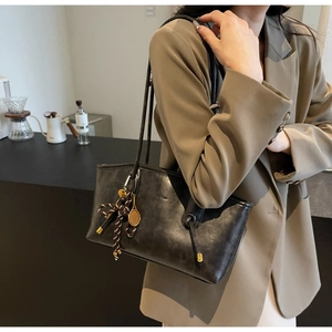 Detail of black vintage leather tote bag featuring a gold tennis racket charm and bow