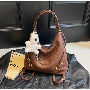 Detail of brown lychee grain PU tote with plush bear pendant on black leather background