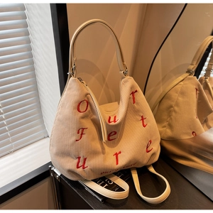 Close-up of beige corduroy tote bag featuring red letter embroidery and faux leather strap
