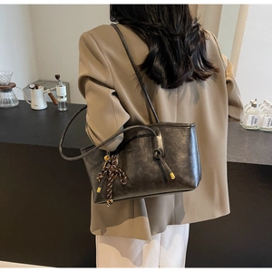 Detailed close-up of dark grey tote bag featuring woven rope charm and leather texture
