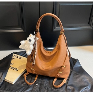 Caramel hobo bag with litchi grain texture and plush bear charm on black leather jacket
