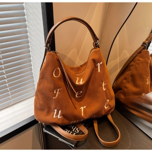 Detail of dark brown corduroy tote with white embroidery and leather handle on a table