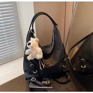 Detail of black pebbled leather tote with gold hardware and white plush dog charm