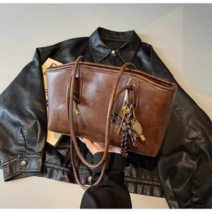 Detail of dark brown leather tote bag with embossed lettering and tennis racket pendant
