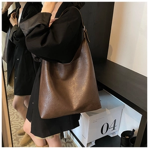 Side view of large brown PU leather tote bag with wide strap on shoulder of a female model