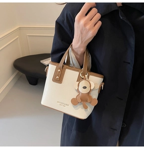 Detail der zweifarbigen Tote-Bag mit Bärenanhänger, getragen von einem Model im Mantel