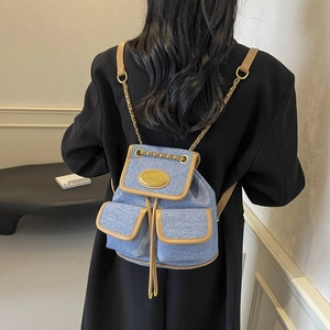 Sac à dos en denim bleu avec bordure en similicuir et chaînes dorées sur un modèle