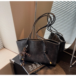 Detail of grey matte tote bag with woven pendant and long straps on a wooden surface