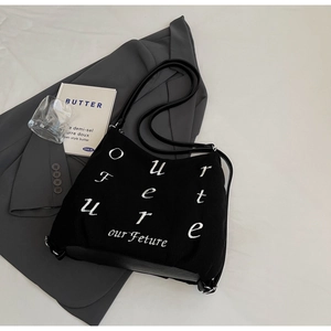 Detail of black corduroy tote with white embroidered lettering on dark grey suit jacket