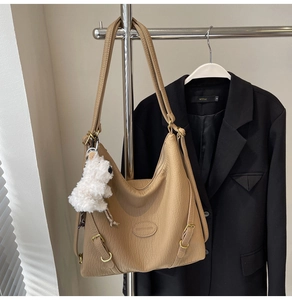 Close-up of khaki textured leather bag with adjustable straps and plush dog charm detail