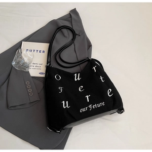 Close-up of black corduroy tote bag featuring white letter embroidery on a grey blazer