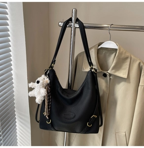 Detail of black textured leather bag with white plush bear charm and fashion label