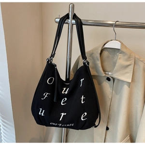 Detail of black corduroy tote bag with white Our Future embroidery on a metal hanger