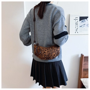 Detail shot of leopard print croissant crossbody bag worn by model in minimalist setting