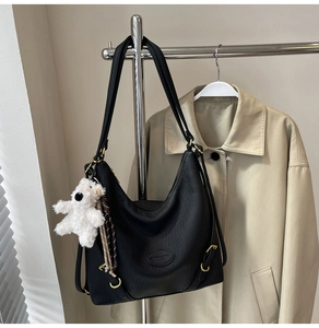 Close-up of black textured leather shoulder bag with gold hardware and plush bear charm