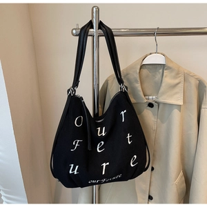 Close-up of black corduroy tote bag featuring white Our Future embroidery and leather straps