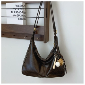 Detail of dark brown hobo bag with adjustable strap and baseball pendant on wood stand