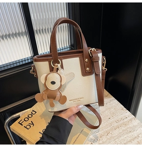 Nahaufnahme der zweifarbigen Handtasche mit Goldlogo und niedlichem Affenanhänger